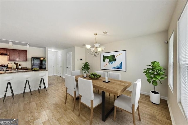 dining space with light wood finished floors, a chandelier, and baseboards