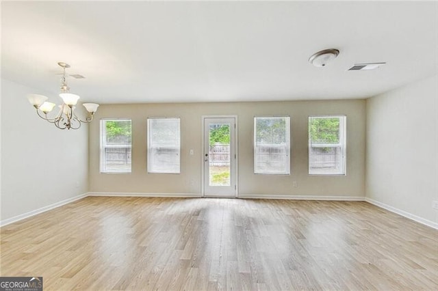 unfurnished living room featuring plenty of natural light, a chandelier, wood finished floors, and baseboards