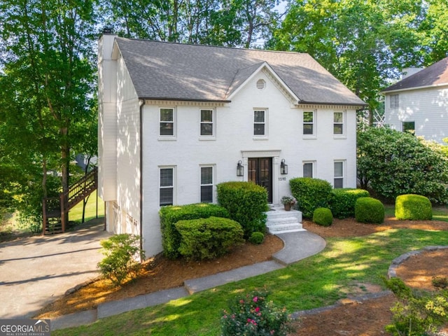 colonial home featuring roof with shingles, brick siding, and driveway