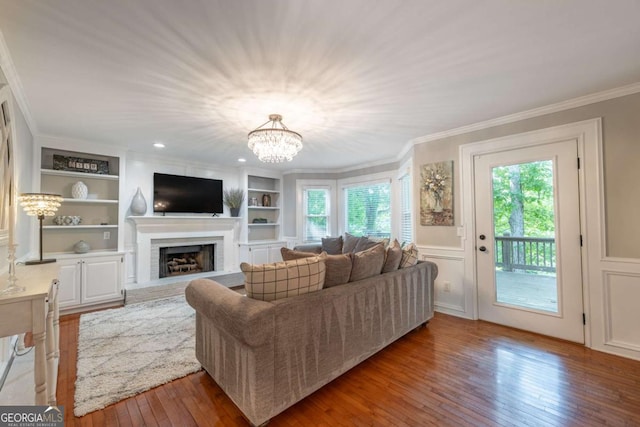 living area featuring wood-type flooring, a fireplace, plenty of natural light, ornamental molding, and built in shelves