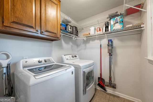 clothes washing area with independent washer and dryer, cabinet space, light tile patterned flooring, and baseboards