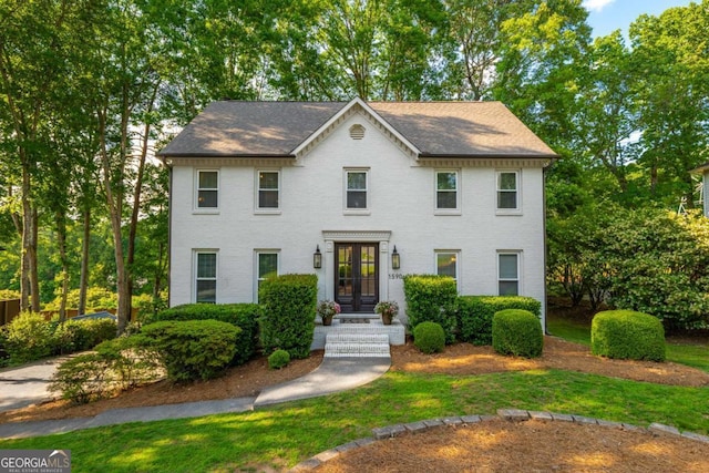 colonial house featuring french doors, brick siding, a front lawn, and a shingled roof