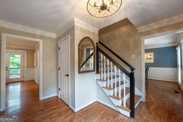 staircase featuring a chandelier, a decorative wall, hardwood / wood-style floors, wainscoting, and ornamental molding