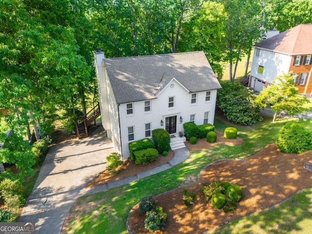 colonial home featuring a chimney, roof with shingles, a front yard, and driveway