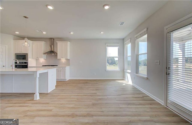 612 Sidney Ct, Stockbridge, GA 30281 - kitchen featuring wall chimney exhaust hood, light countertops, stainless steel microwave, white cabinetry, and light wood finished floors