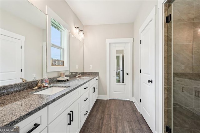 bathroom featuring wood finished floors, double vanity, tiled shower, and baseboards