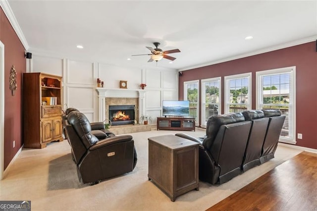 living area featuring a ceiling fan, a tiled fireplace, ornamental molding, recessed lighting, and light wood-style flooring