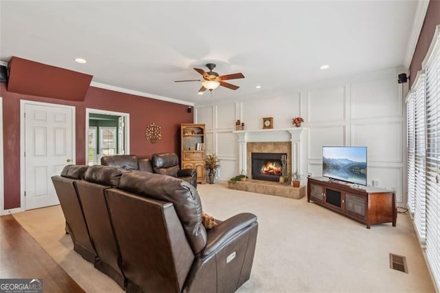 living room featuring a decorative wall, a ceiling fan, ornamental molding, and a fireplace