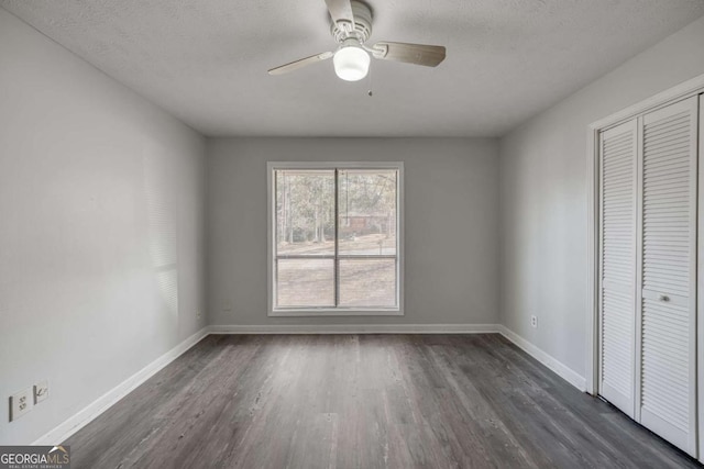 unfurnished bedroom featuring a closet, dark wood-style floors, baseboards, ceiling fan, and a textured ceiling