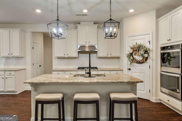 2046 Yvette Way, Braselton, GA 30517 - kitchen featuring double oven, a chandelier, under cabinet range hood, a kitchen breakfast bar, and recessed lighting