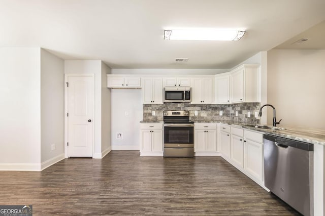 kitchen featuring appliances with stainless steel finishes, a sink, tasteful backsplash, dark wood-style flooring, and white cabinetry