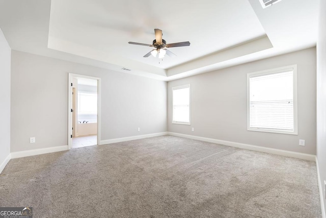 carpeted empty room featuring a raised ceiling, ceiling fan, and baseboards