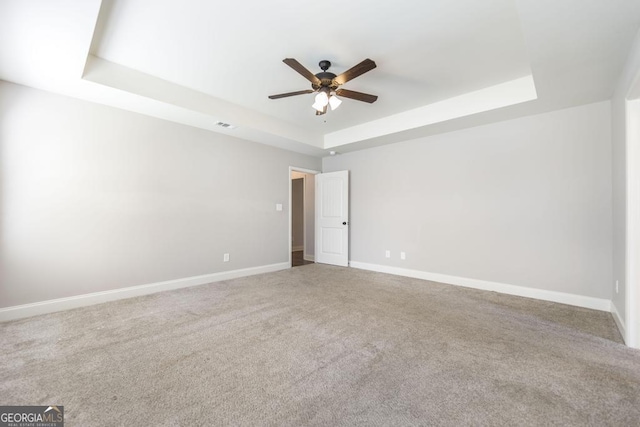 carpeted empty room featuring a tray ceiling, ceiling fan, and baseboards