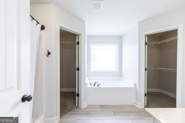bathroom with a bath, baseboards, and a walk in closet