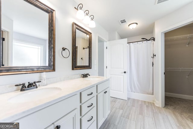 bathroom featuring a shower with curtain, double vanity, a walk in closet, and baseboards