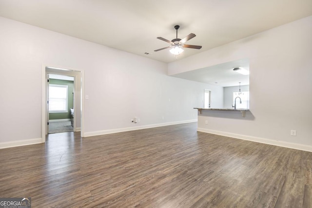 unfurnished living room with dark wood finished floors, a ceiling fan, baseboards, and a sink