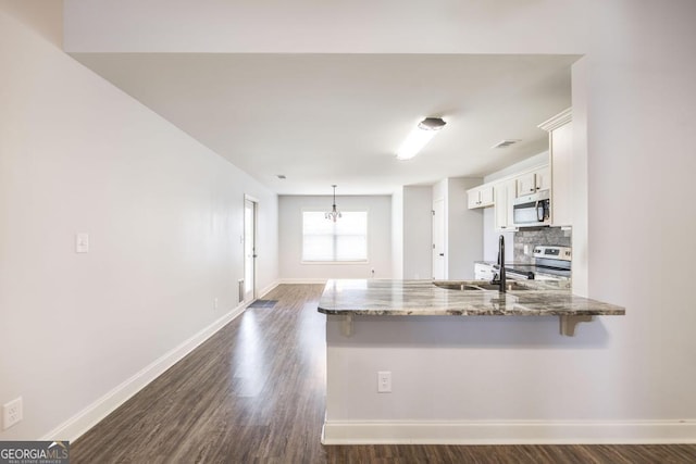 kitchen featuring appliances with stainless steel finishes, white cabinetry, a sink, a peninsula, and a kitchen bar