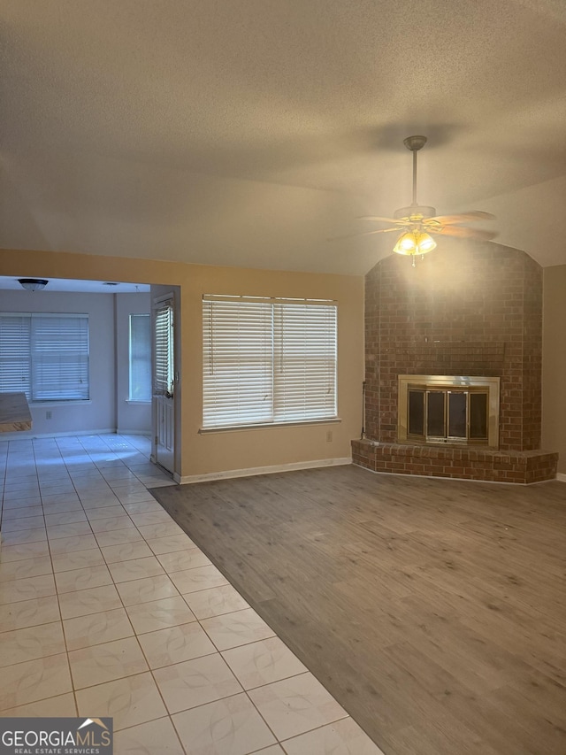 unfurnished living room with a ceiling fan, a brick fireplace, a textured ceiling, baseboards, and vaulted ceiling