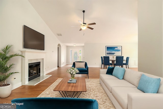 living area featuring a ceiling fan, wood finished floors, arched walkways, lofted ceiling, and a premium fireplace