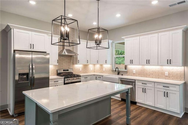 kitchen featuring stainless steel appliances, a sink, a kitchen island, light countertops, and hanging light fixtures