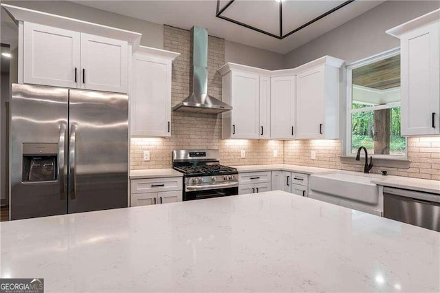 kitchen with appliances with stainless steel finishes, wall chimney exhaust hood, a sink, light stone countertops, and tasteful backsplash