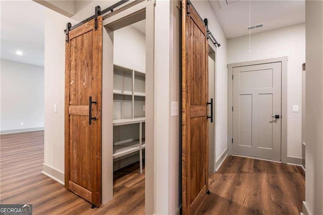 hallway featuring a barn door, wood finished floors, baseboards, and recessed lighting