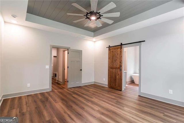 empty room featuring a tray ceiling, a barn door, ceiling fan, wood finished floors, and wood ceiling