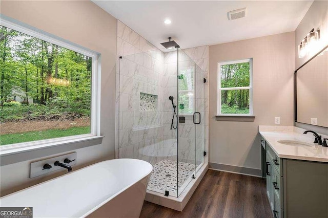 bathroom with a stall shower, vanity, wood finished floors, a freestanding bath, and baseboards