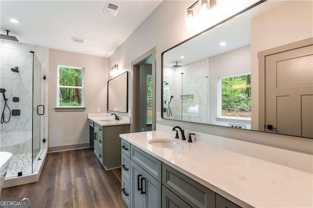 bathroom featuring a shower stall, wood finished floors, two vanities, baseboards, and recessed lighting