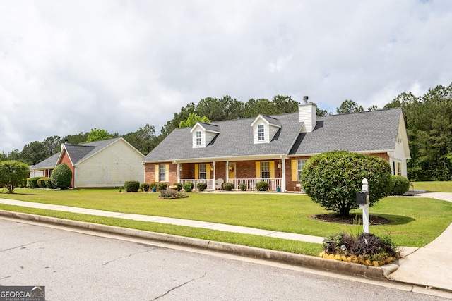 new england style home featuring a porch, brick siding, a front lawn, and a chimney