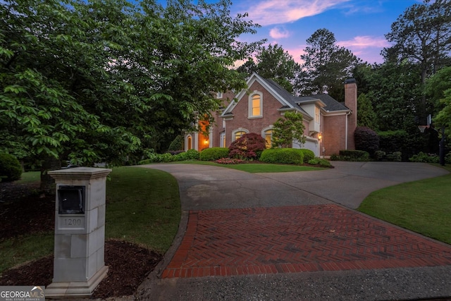 view of front of property with curved driveway, a chimney, and brick siding