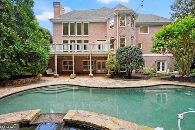 back of property with a chimney, brick siding, an outdoor pool, french doors, and a patio area