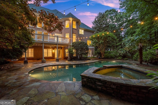 pool at dusk with a patio area and a pool with connected hot tub