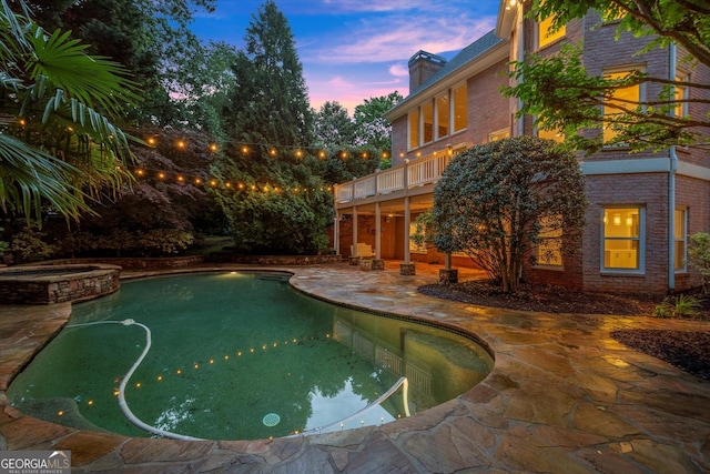 pool at dusk featuring a patio and a pool with connected hot tub