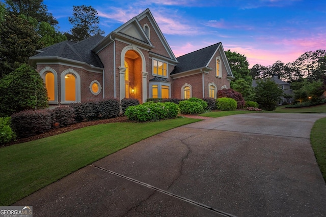 view of front of property featuring brick siding, a lawn, concrete driveway, and a shingled roof