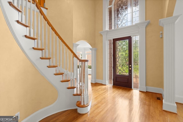 entryway with arched walkways, a high ceiling, wood finished floors, stairway, and baseboards