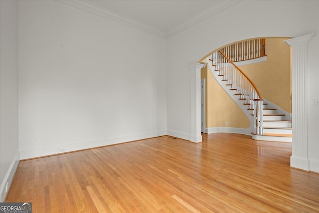spare room featuring arched walkways, wood finished floors, ornate columns, stairway, and baseboards