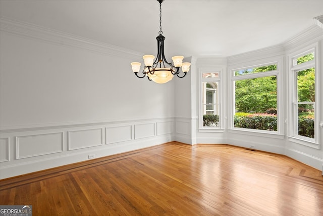 empty room with a chandelier, ornamental molding, and wood finished floors