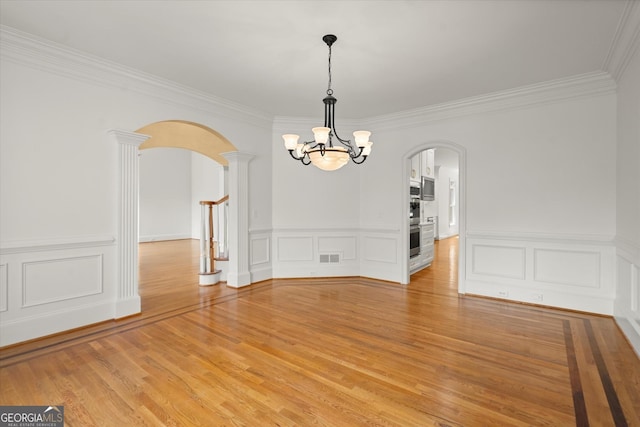 unfurnished dining area with arched walkways, a chandelier, crown molding, light wood finished floors, and a decorative wall