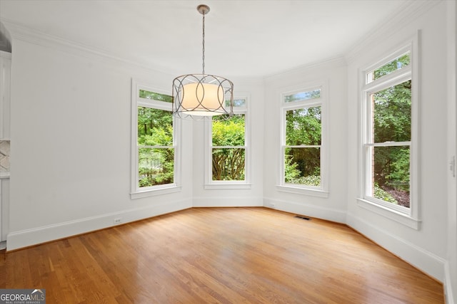 unfurnished dining area featuring light wood-style floors, ornamental molding, baseboards, and a chandelier