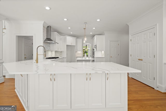kitchen featuring wall chimney range hood, crown molding, light wood finished floors, white cabinets, and light stone countertops