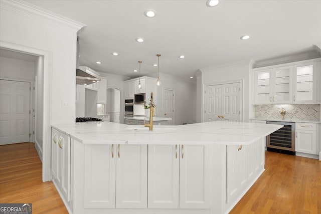 kitchen featuring beverage cooler, a peninsula, stainless steel microwave, white cabinetry, and crown molding