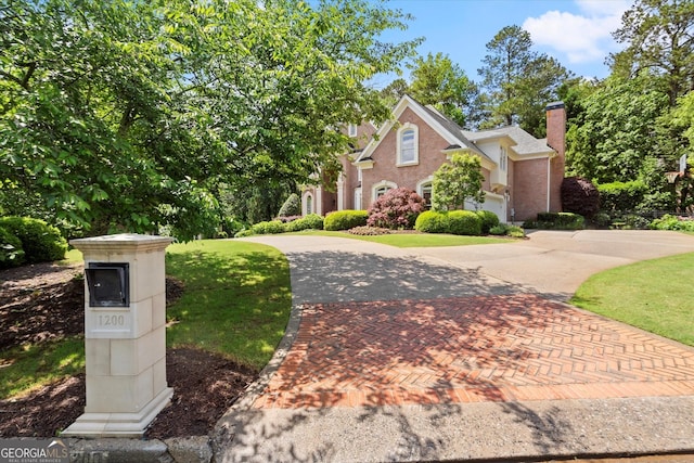 view of front of home featuring curved driveway, a chimney, a front yard, and brick siding