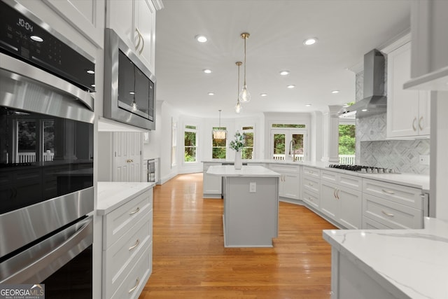 kitchen with wall chimney range hood, appliances with stainless steel finishes, light wood-style floors, recessed lighting, and white cabinets