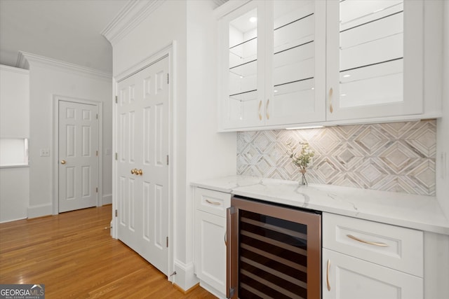 indoor dry bar with wine cooler, crown molding, backsplash, light wood-type flooring, and baseboards