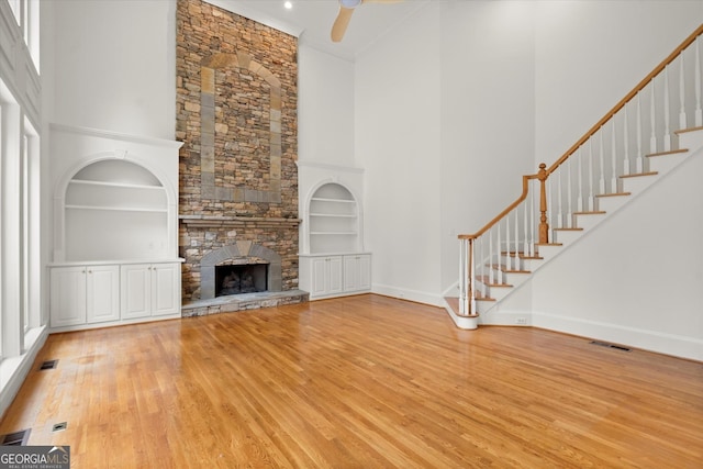 unfurnished living room featuring a towering ceiling, wood finished floors, built in features, a ceiling fan, and baseboards