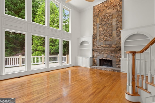unfurnished living room with wood finished floors, a ceiling fan, built in shelves, a stone fireplace, and a high ceiling