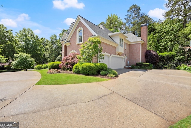 view of home's exterior with concrete driveway, a chimney, brick siding, a yard, and an attached garage