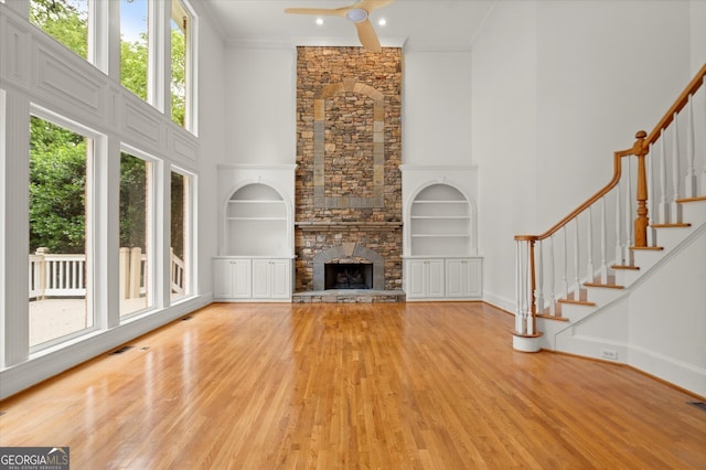unfurnished living room featuring built in shelves, a towering ceiling, healthy amount of natural light, wood finished floors, and stairway