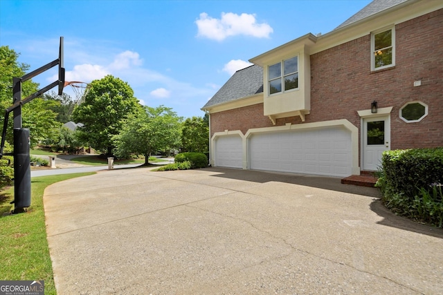 view of side of home with driveway, brick siding, and roof with shingles